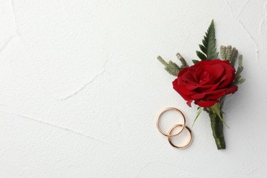 Photo of Stylish red boutonniere and rings on white textured table, top view. Space for text