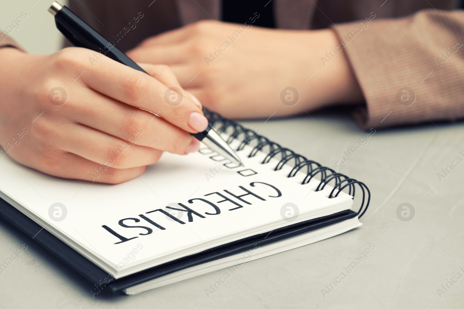 Photo of Woman filling Checklist at light grey table, closeup