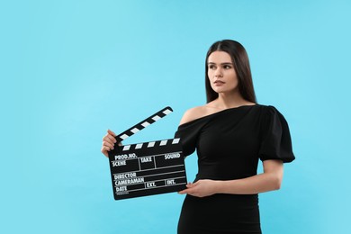 Actress with clapperboard on light blue background, space for text. Film industry