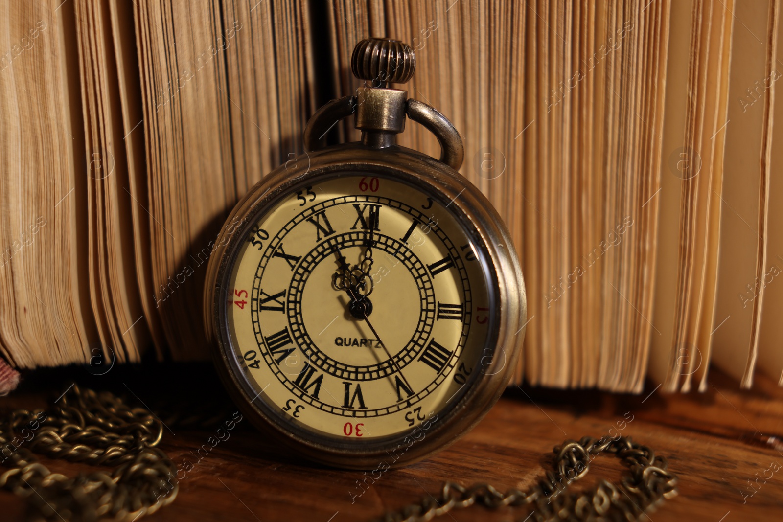 Photo of Pocket clock with chain and book on wooden table, closeup