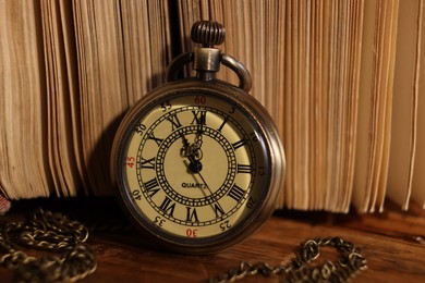 Pocket clock with chain and book on wooden table, closeup