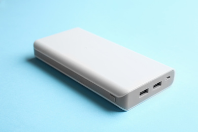 Photo of Modern external portable charger on light blue background, closeup