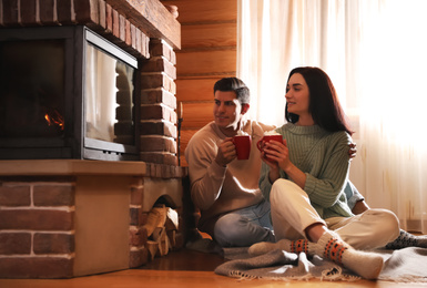 Photo of Lovely couple with delicious cocoa near fireplace on floor at home. Winter vacation