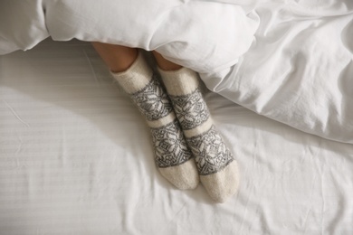 Photo of Woman wearing knitted socks under blanket in bed, top view