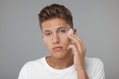 Photo of Handsome man cleaning face with cotton pad on grey background