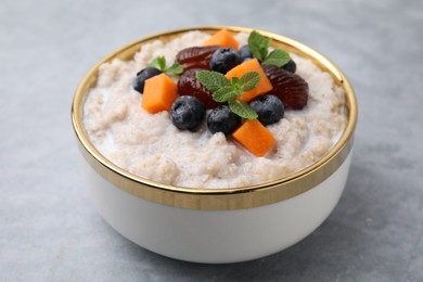 Photo of Delicious barley porridge with blueberries, pumpkin, dates and mint in bowl on grey table, closeup