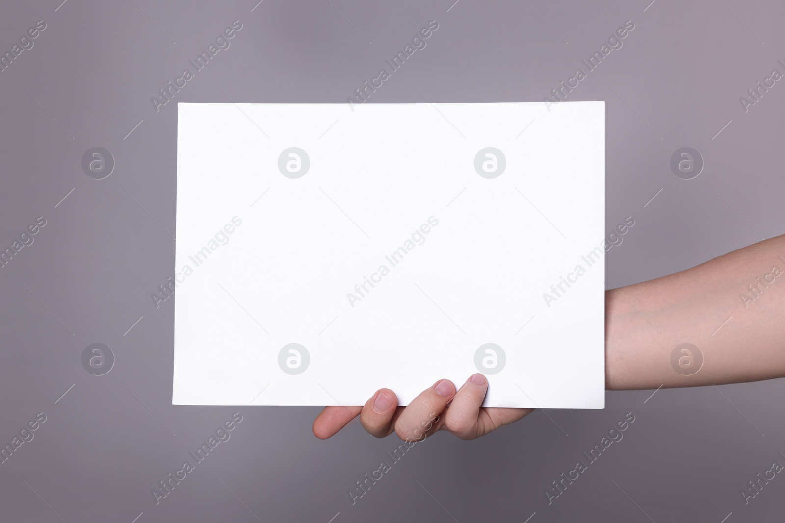 Photo of Woman holding sheet of paper on grey background, closeup. Mockup for design