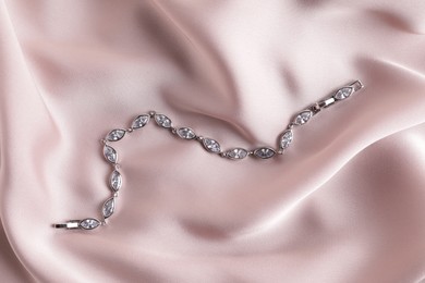 Photo of Elegant jewelry. Luxury bracelet on pink silk cloth, top view