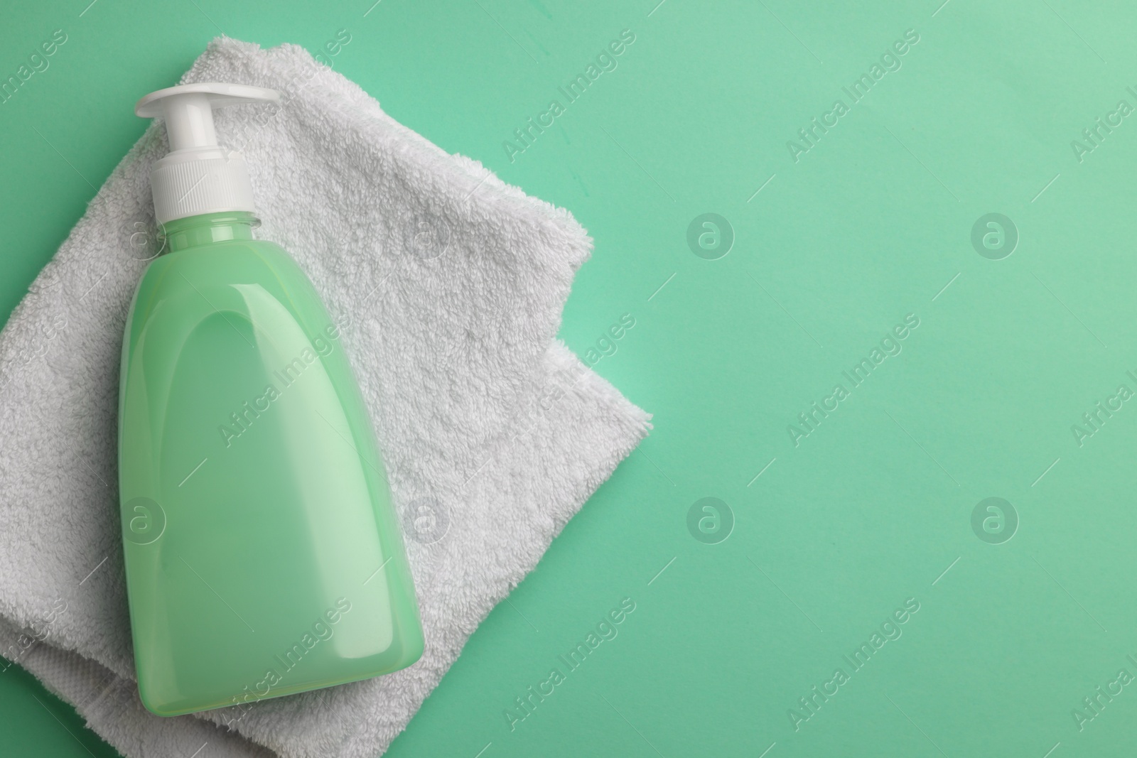 Photo of Bottle of liquid soap and towel on turquoise background, top view. Space for text