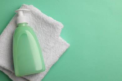 Bottle of liquid soap and towel on turquoise background, top view. Space for text