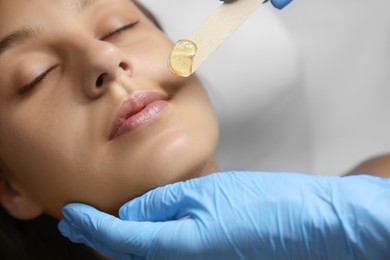 Photo of Young woman undergoing hair removal procedure on face with sugaring paste in salon, closeup
