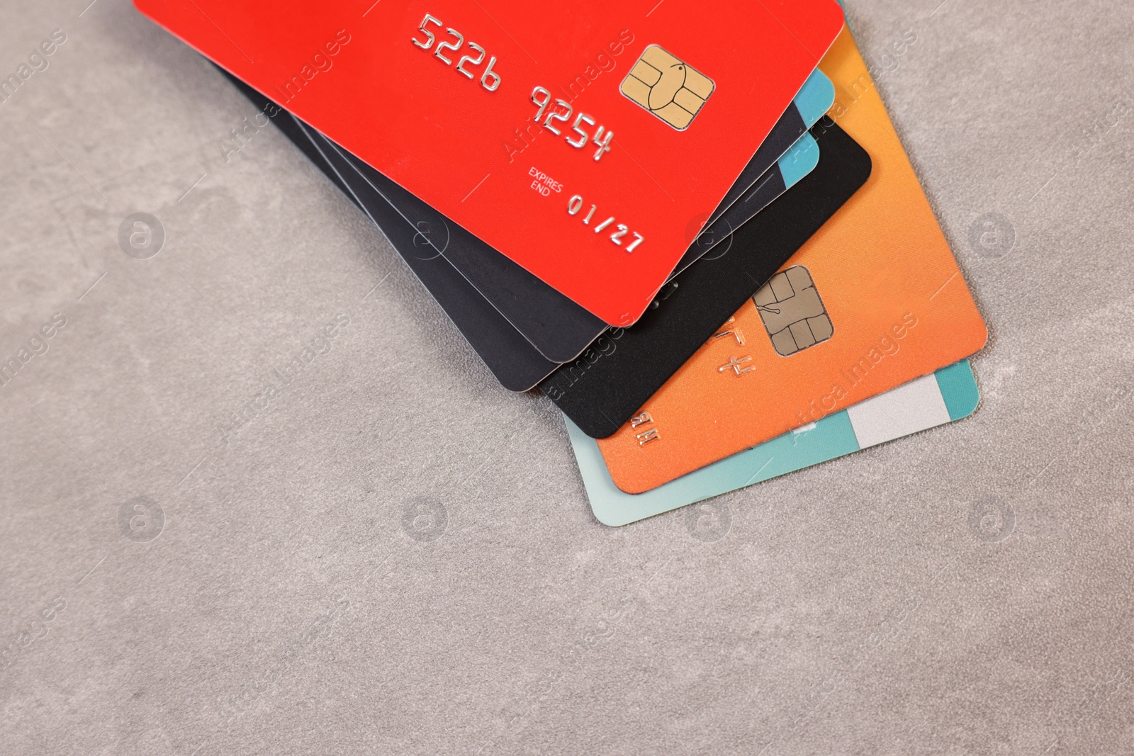 Photo of Pile of different credit cards on grey table, top view. Space for text