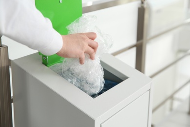 Photo of Young woman throwing plastic film in metal bin indoors, closeup. Waste recycling
