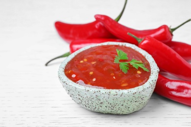 Photo of Bowl of hot chili sauce with parsley on table, closeup