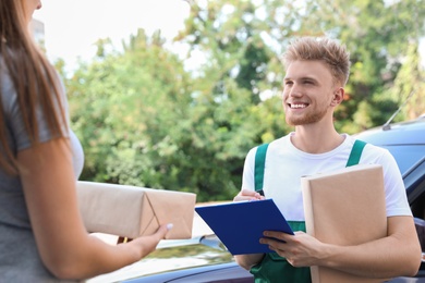 Young delivery courier with clipboard giving parcels to customer outdoors