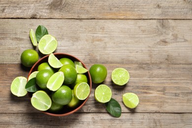 Photo of Tasty ripe limes in bowl on wooden table, top view. Space for text