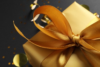 Golden gift box with bow on black background, closeup
