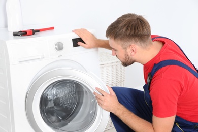 Young plumber examining washing machine in bathroom