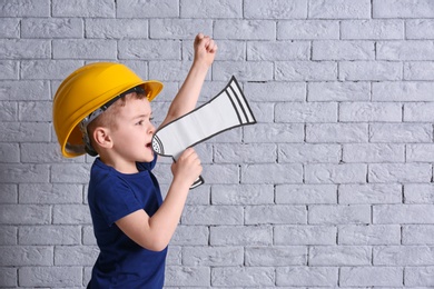 Photo of Adorable little boy in hardhat with paper megaphone on brick wall background