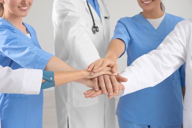 Photo of Team of medical doctors putting hands together indoors, closeup