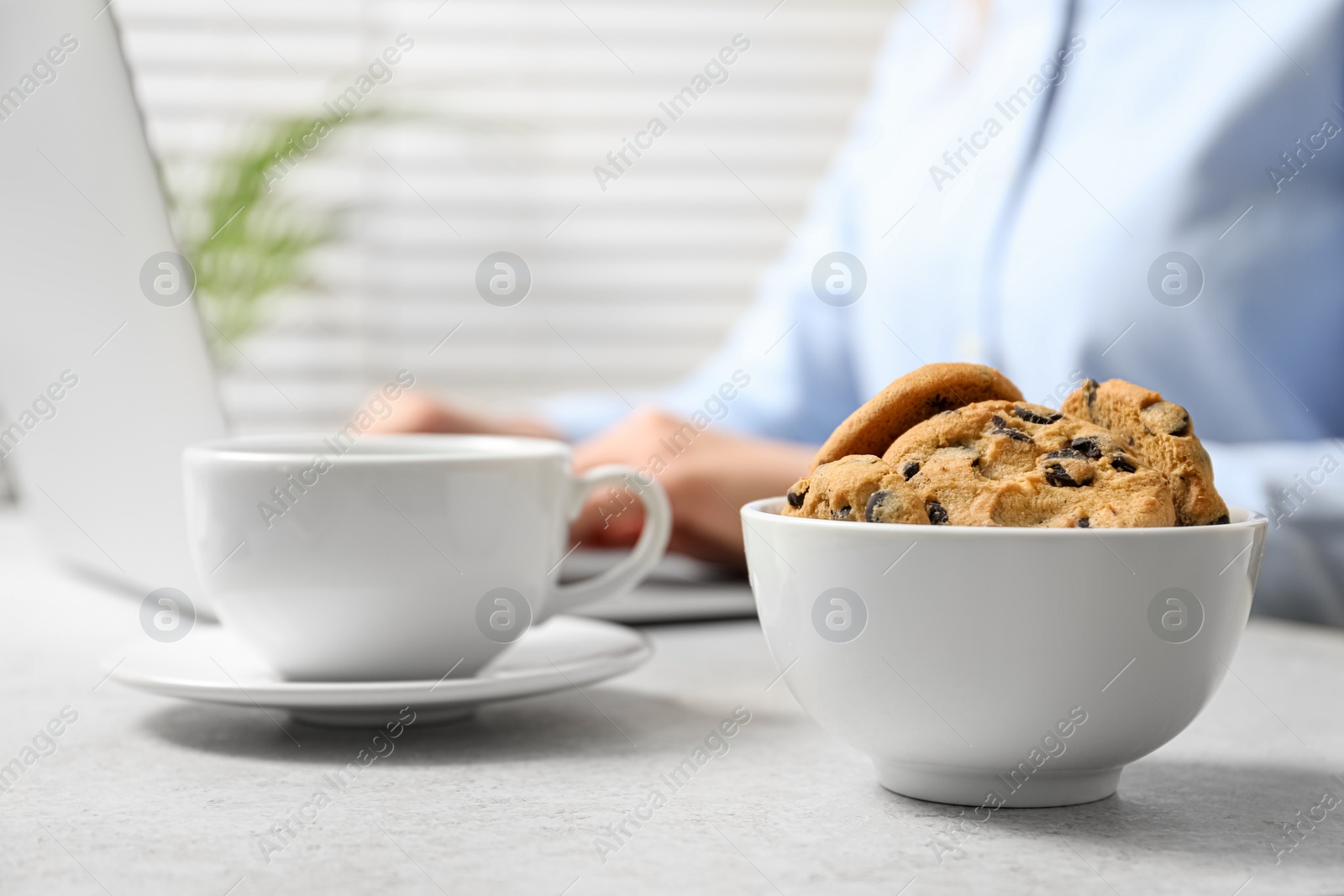 Photo of Chocolate chip cookies with cup of drink on table and office worker on background, closeup