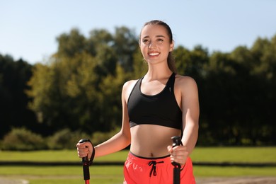 Happy woman practicing Nordic walking with poles in park on sunny day