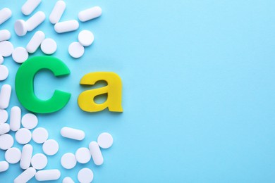 Photo of Calcium symbol made of colorful letters and white pills on light blue background, flat lay. Space for text
