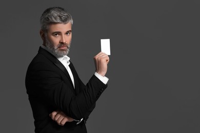 Photo of Handsome businessman holding blank business card on grey background. Space for text