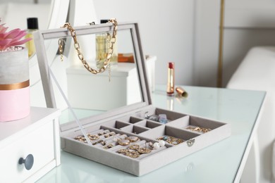 Photo of Elegant jewelry box with beautiful bijouterie, cosmetics and stylish accessories on dressing table in room