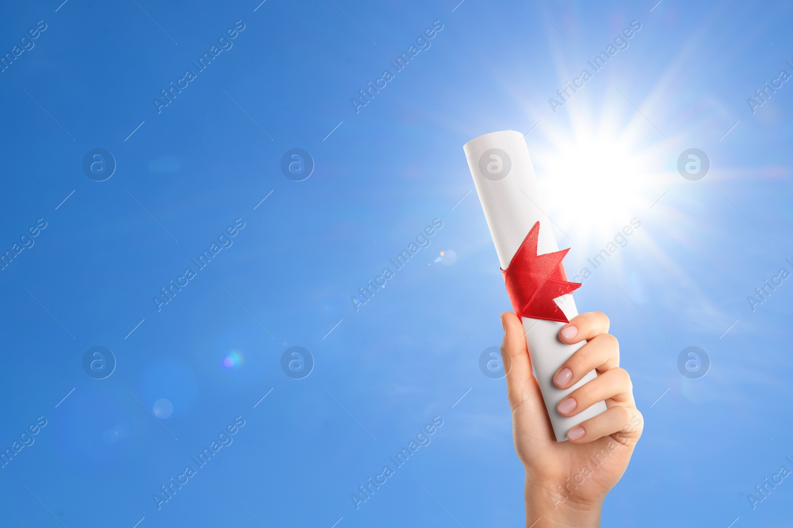 Image of Graduated student holding diploma against blue sky on sunny day, closeup