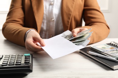 Money exchange. Woman putting dollar banknotes into envelope at white wooden table, closeup