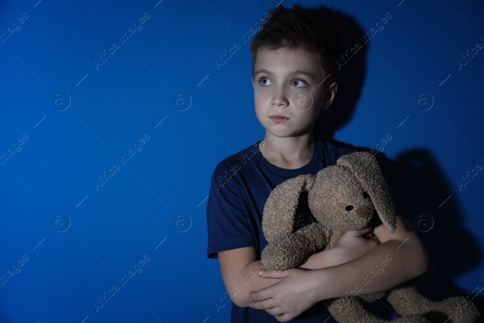 Photo of Sad little boy with toy near blue wall, space for text. Domestic violence concept