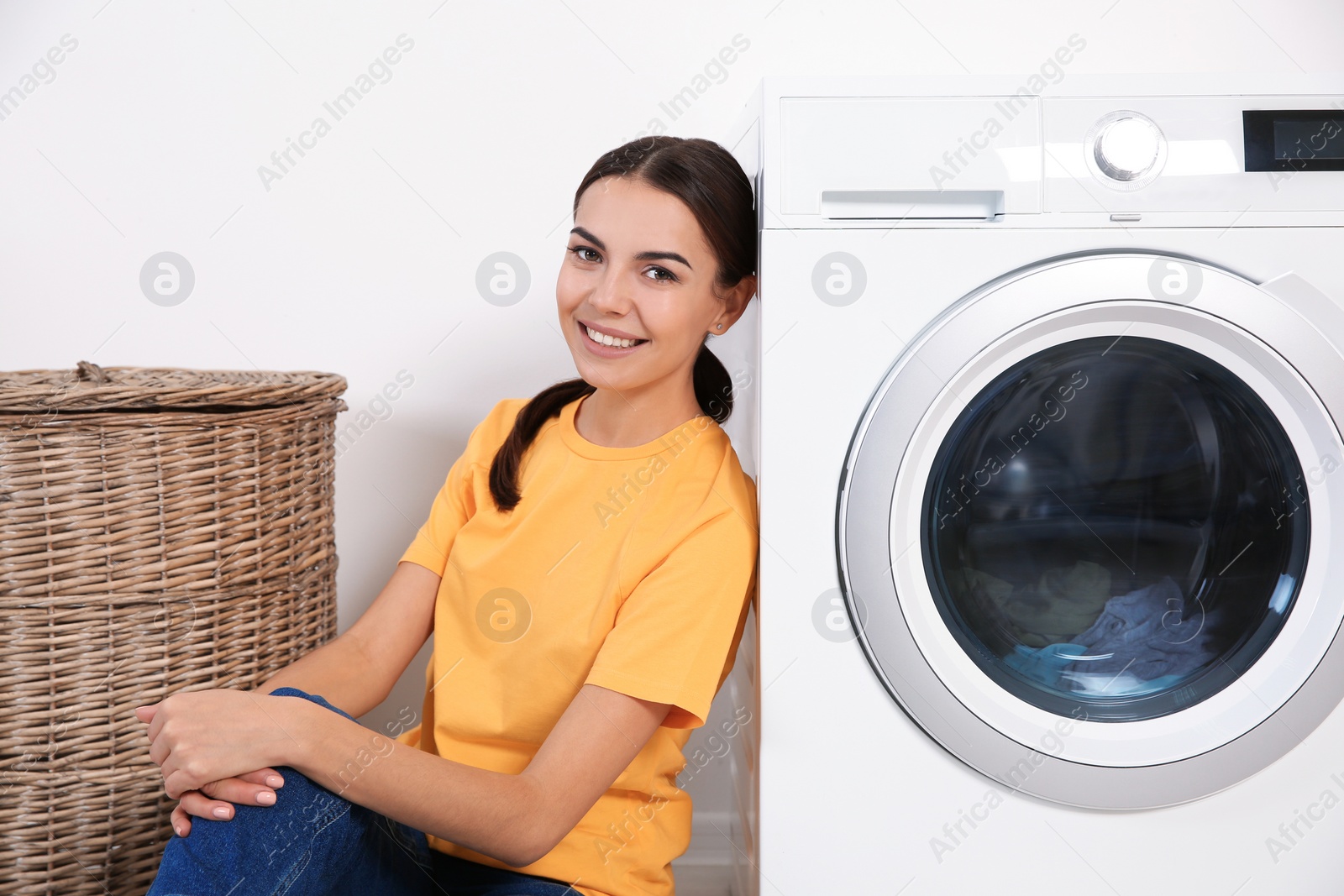 Photo of Young woman near washing machine at home. Laundry day