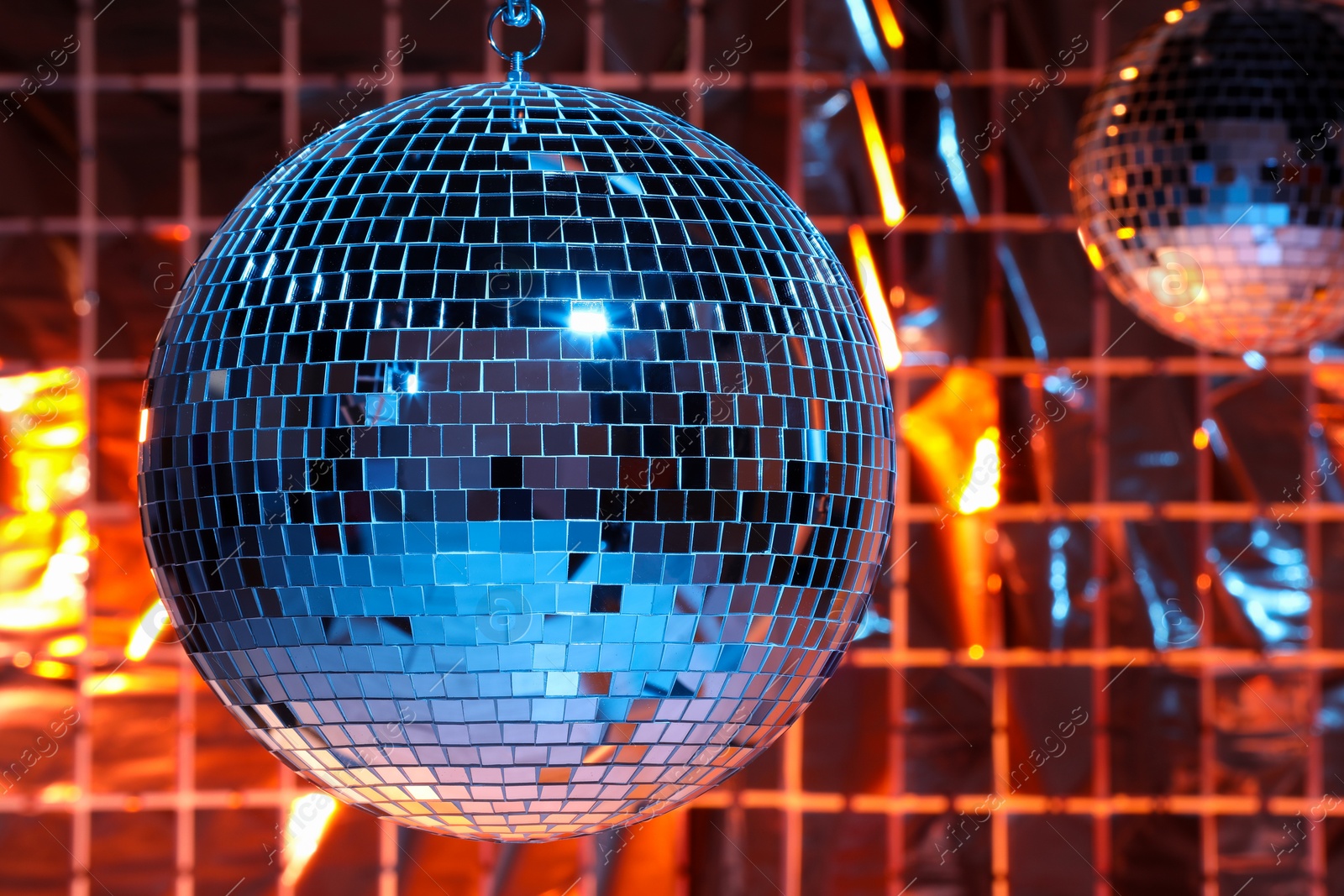 Photo of Shiny disco balls against foil party curtain under color lights