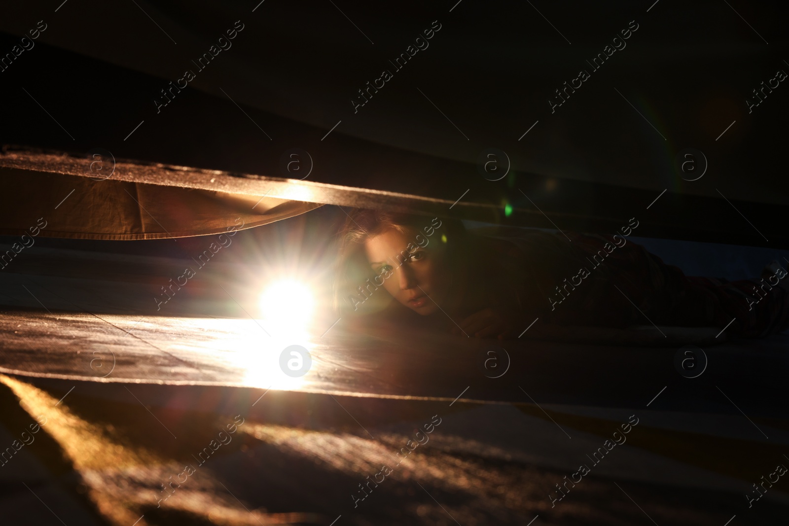 Photo of Little girl with flashlight looking for monster under bed at night