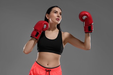 Beautiful woman in boxing gloves on grey background, low angle view