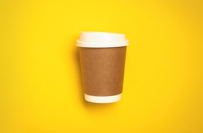 Takeaway paper coffee cup on yellow background, top view