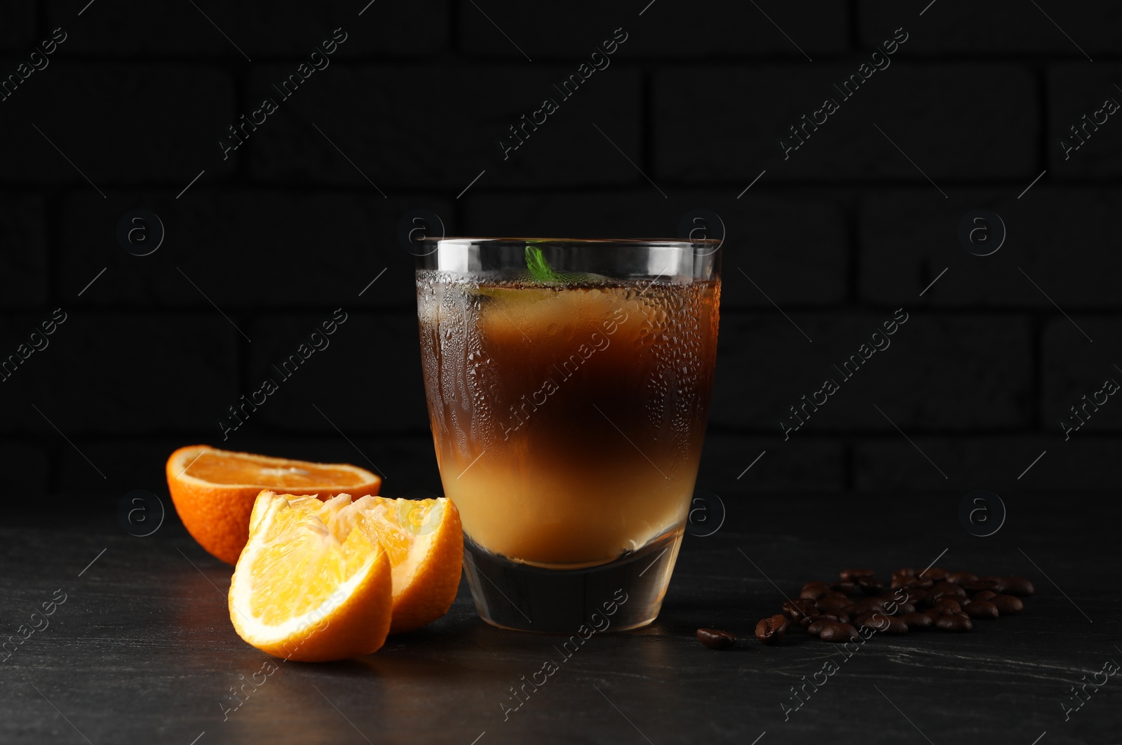 Photo of Tasty refreshing drink with coffee and orange juice on grey table against dark background