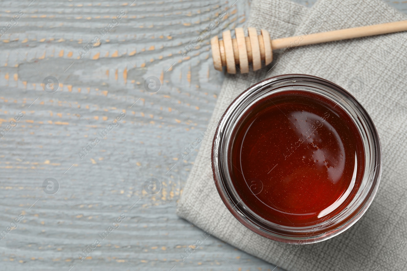 Photo of Glass jar with tasty honey and dipper on grey table, top view. Space for text