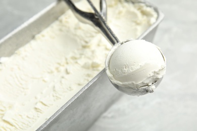 Container and scoop with delicious vanilla ice cream on table, closeup