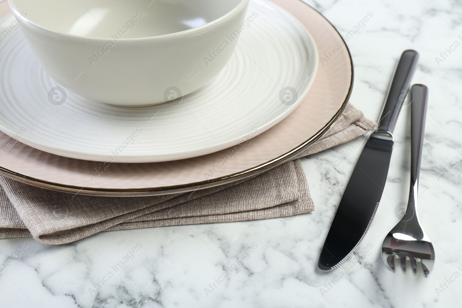 Photo of Clean plates, bowl, cutlery and napkin on white marble table, closeup