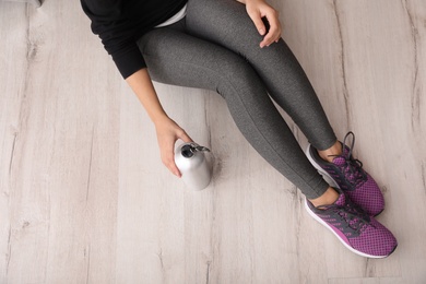 Woman in sportswear with bottle of water sitting on floor indoors, top view. Space for text