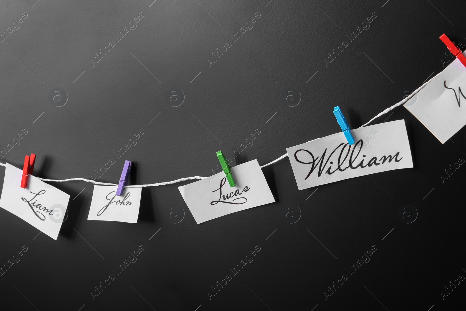 Photo of Paper pieces with baby names on rope against black background, closeup
