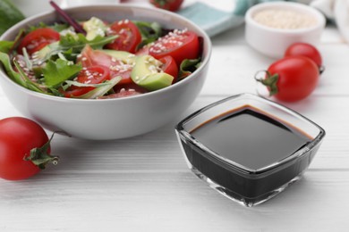 Tasty soy sauce, bowl with salad and ingredients on white wooden table, closeup