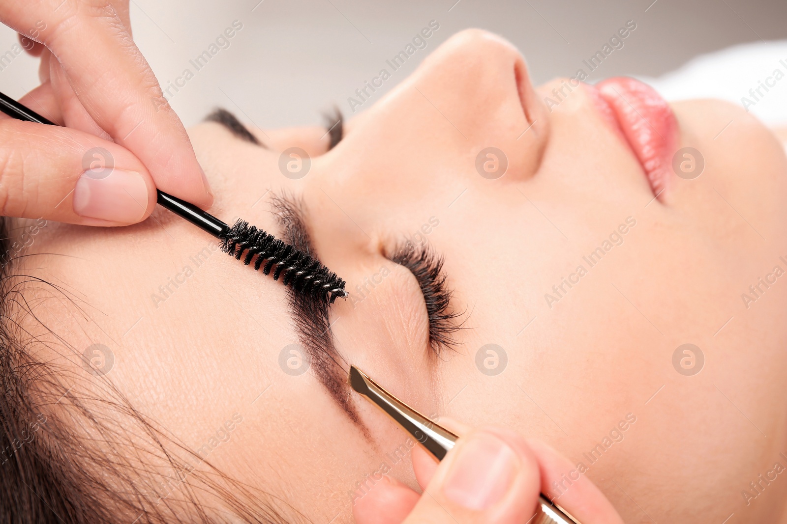 Photo of Young woman having professional eyebrow correction procedure in beauty salon, closeup