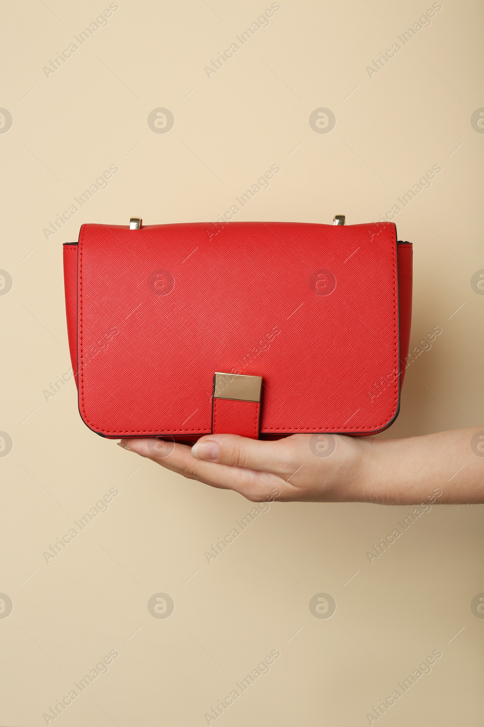Photo of Woman holding stylish red bag on beige background, closeup