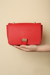 Woman holding stylish red bag on beige background, closeup