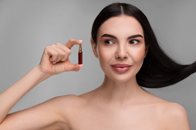 Photo of Beautiful young woman with long healthy hair holding ampoule on grey background