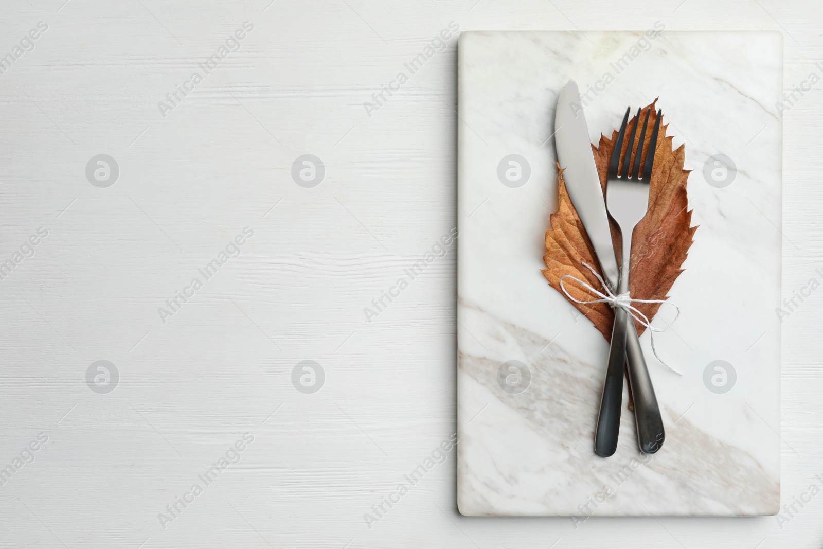 Photo of Cutlery, dry leaf and marble board on white wooden background, top view with space for text. Table setting elements