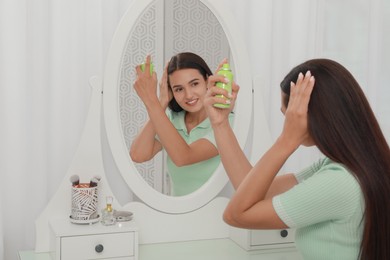 Photo of Woman applying dry shampoo onto her hair near mirror at home